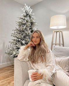 a woman sitting on a couch in front of a christmas tree holding a coffee cup