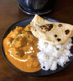 a black plate topped with rice and curry next to a tortilla covered in sauce