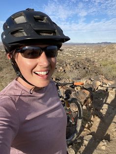 a woman wearing a helmet and sunglasses on top of a dirt field next to a bike