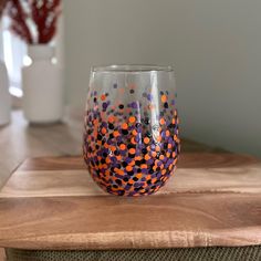 a wine glass with orange, purple and black dots on it sitting on top of a wooden table