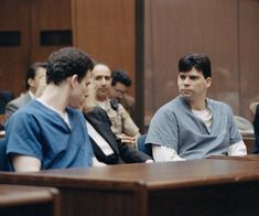 three men sitting at a table in front of a group of other people, all wearing scrubs