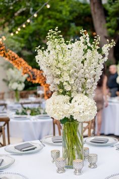 a vase filled with white flowers sitting on top of a table covered in plates and napkins