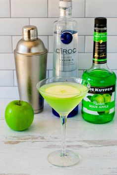 an apple martini is garnished with limes, vodka and two bottles in the background