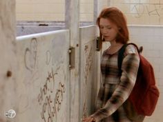 a woman with red hair is standing in front of a door and looking at something on the wall