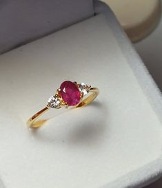 a gold ring with two diamonds and a pink stone in it's center sitting on a white box