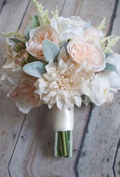 a bridal bouquet with white flowers and greenery on a wooden floor in front of a brick wall