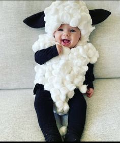 a baby wearing a sheep costume sitting on top of a white couch with his mouth open