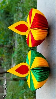 two colorful paper umbrellas hanging on the side of a building in front of trees