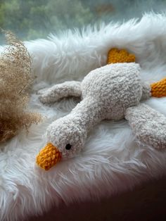 a stuffed bird laying on top of a fluffy white blanket next to a teddy bear