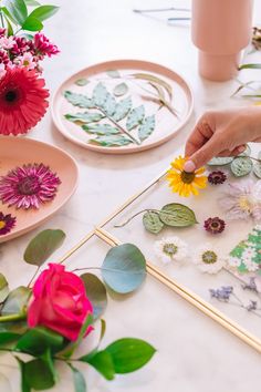 a table topped with plates and flowers on top of a white countertop next to pink vases