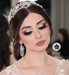 a woman wearing a tiara and makeup looks down at her face with eyes closed