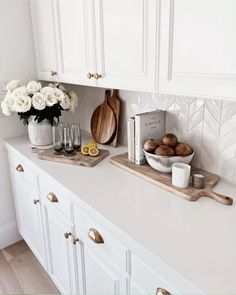 a kitchen counter with white cabinets and flowers in vases on the counter top next to cutting board