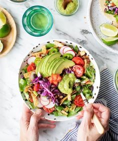 a person holding a bowl of salad with avocado, tomatoes, onions and lettuce