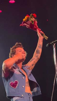 a man holding flowers up to his face while standing in front of a microphone on stage