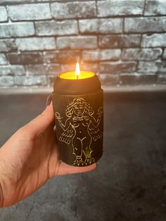 a hand holding a lit candle in front of a brick wall with an angel on it