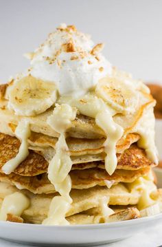 a white plate topped with pancakes covered in bananas and whipped cream