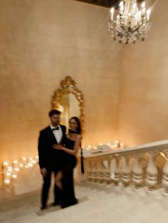 a man and woman standing next to each other in front of a chandelier