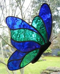 a stained glass butterfly sitting on top of a window sill next to a tree