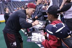 a young man signing autographs for fans at a baseball game with other people in the stands