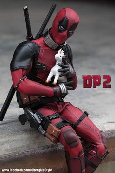 a deadpool doll is sitting on a ledge and holding a small white dog in his arms