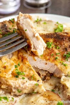 a close up of a plate of food with meat and potatoes on it, with a fork in the middle