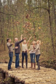 a group of people standing on top of a wooden bridge in the woods throwing leaves into the air