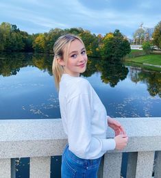 a girl standing on a bridge looking at the camera with her hands in her pockets