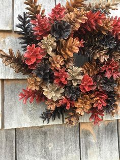 a wreath made out of pine cones and red berries on a wooden wall with leaves