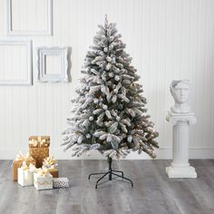 a white christmas tree with presents under it on the floor in front of a wall