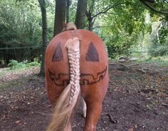 a horse with two braids on it's back walking through the woods in front of some trees