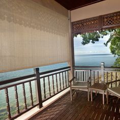 two chairs sitting on top of a wooden deck next to the ocean with an open window