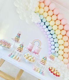 a table topped with lots of desserts and balloons in front of a rainbow wall