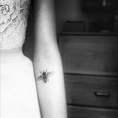 a black and white photo of a woman's arm with a bee tattoo on it