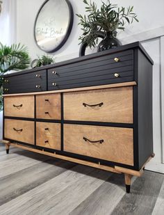 a black and wood dresser sitting on top of a hard wood floor next to a potted plant