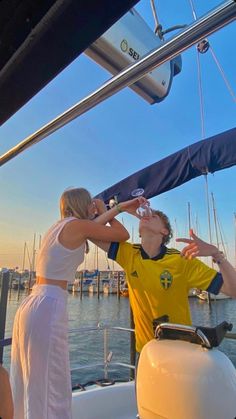 two people standing on the deck of a boat drinking from wine glasses while another person holds his hand up