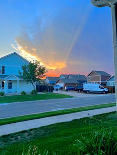 the sun is setting over some houses and lawns in front of an empty street