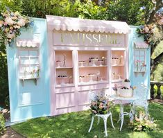 a pink and blue booth with flowers on the front, chairs and tables outside in the grass