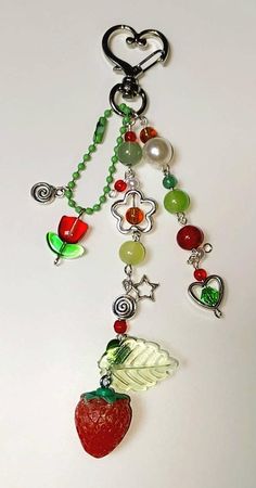 a red strawberry hanging from a chain with beads and charms on it's end