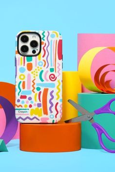 a cell phone case sitting on top of some colorful boxes with scissors next to it