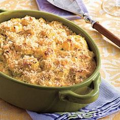 a green casserole dish with cheese and bread crumbs in it on a yellow table cloth