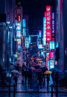 many people with umbrellas are walking down the street in the city at night time