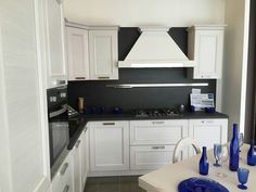 a kitchen with white cabinets and blue glassware on the counter top, in front of an oven