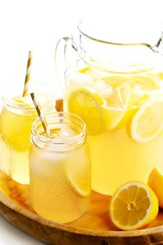 two mason jars filled with lemonade and sliced lemons on a wooden platter