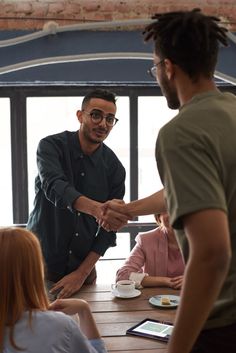 two men shaking hands over a wooden table with people sitting around it in front of them