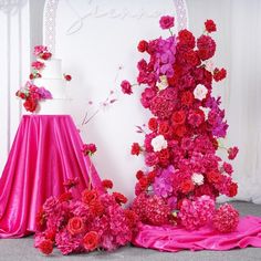 a wedding cake with pink and red flowers on it, next to a table cloth