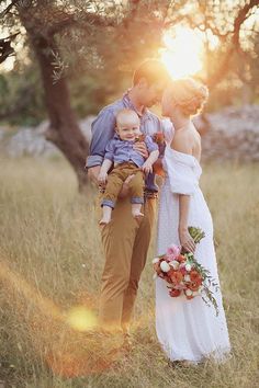 a man and woman holding a baby in their arms while standing in a field with the sun behind them