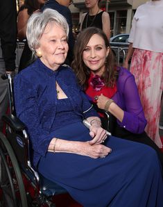 an older woman sitting in a wheel chair next to a younger woman on the red carpet