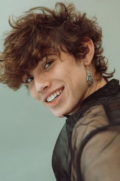 a close up of a person with curly hair and blue eyes smiling at the camera