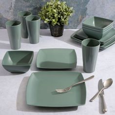 a table set with green dishes, silverware and a potted plant in the background