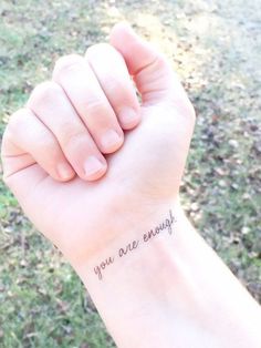 a woman's wrist with the words you are enough written on her left arm